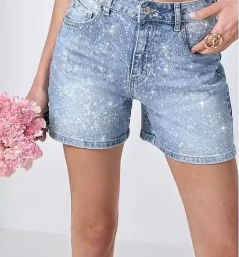 Pantaloncini di jeans azzurri con lavaggio effetto usurato, indossati con una mano in tasca e fiori rosa sul lato.