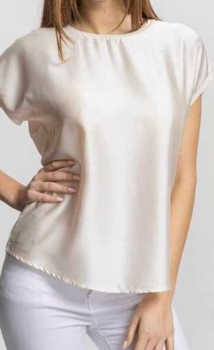 Camicetta bianca a maniche corte con drappeggio e orlo ampio, indossata da una modella con pantaloni bianchi su sfondo neutro.