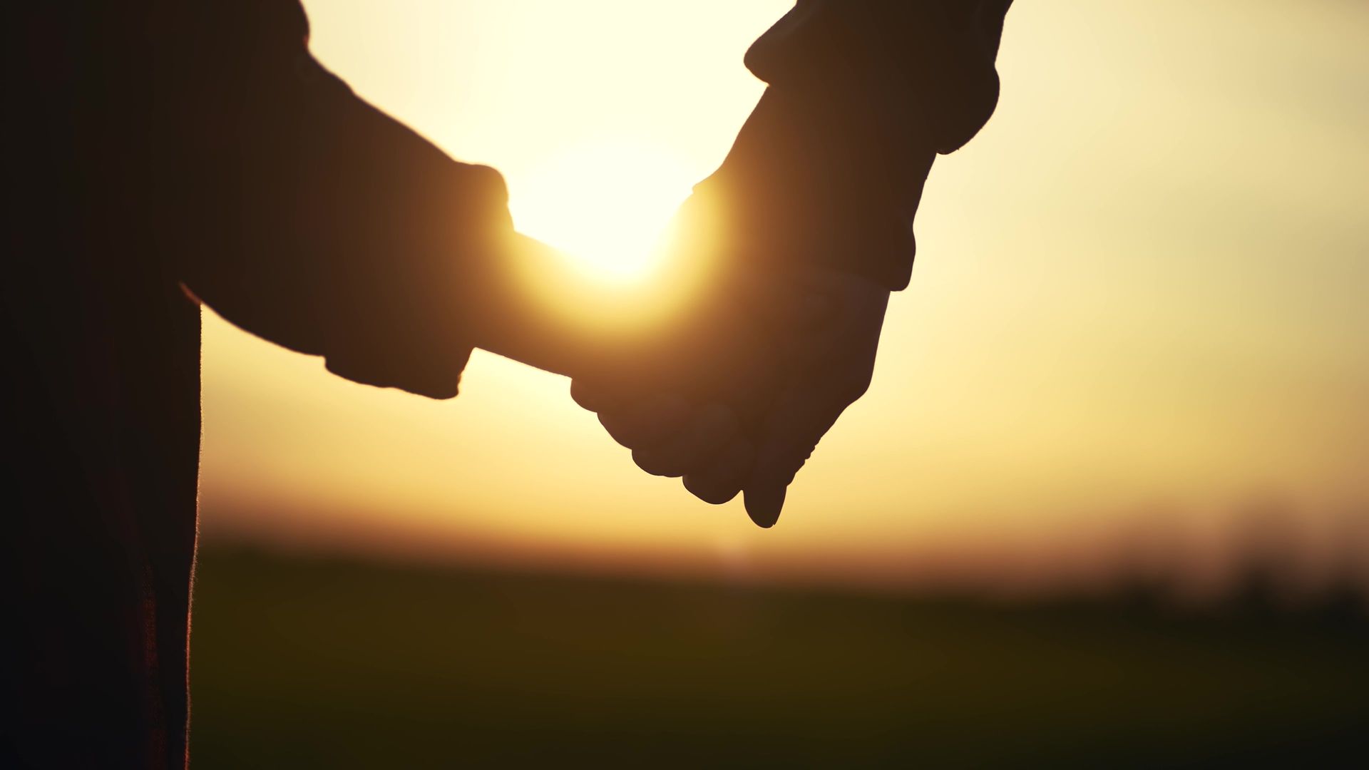 Two silhouetted hands holding at sunset, with warm golden light in the background