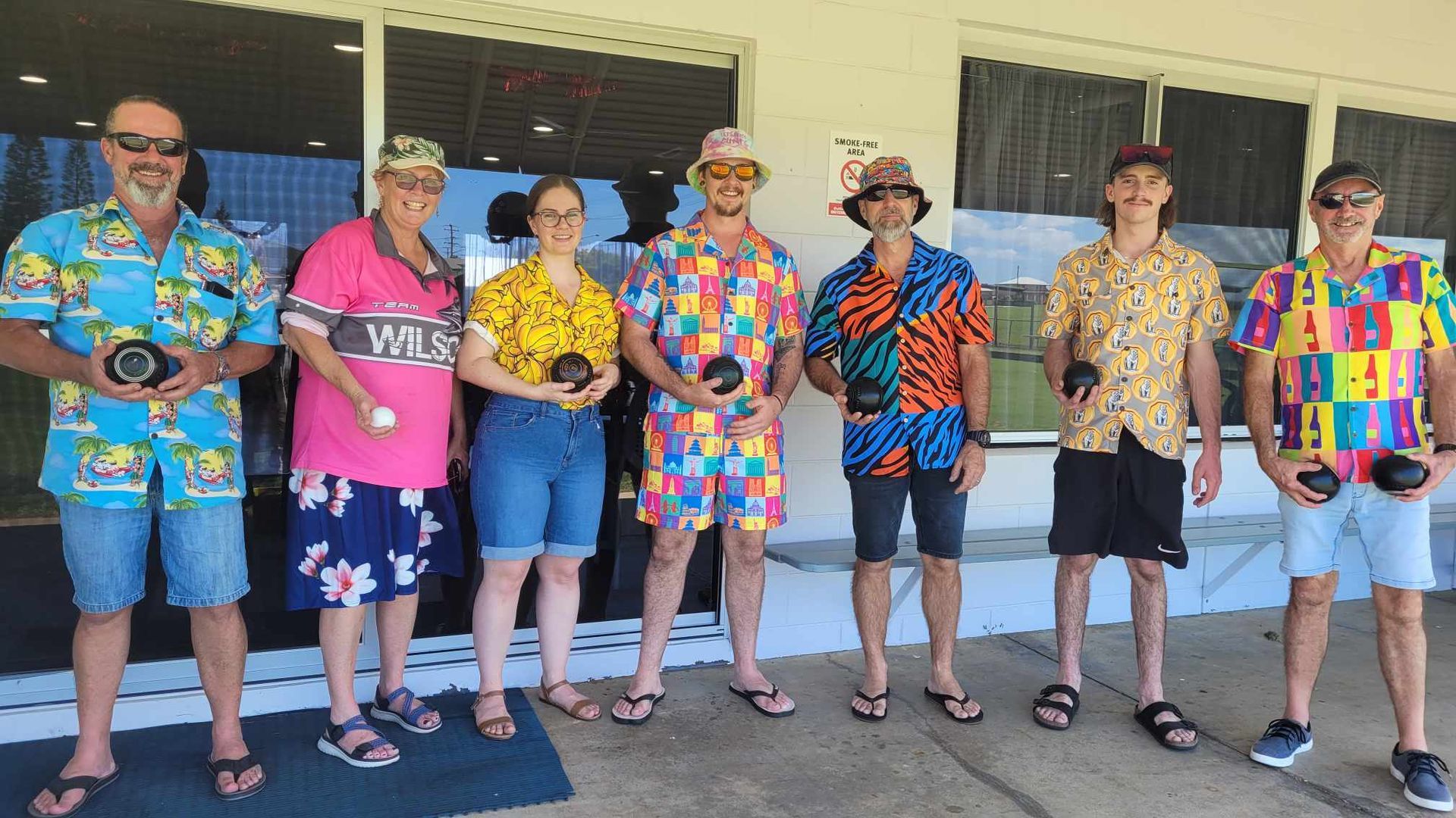 A group of people wearing colorful shirts are standing in front of a building.