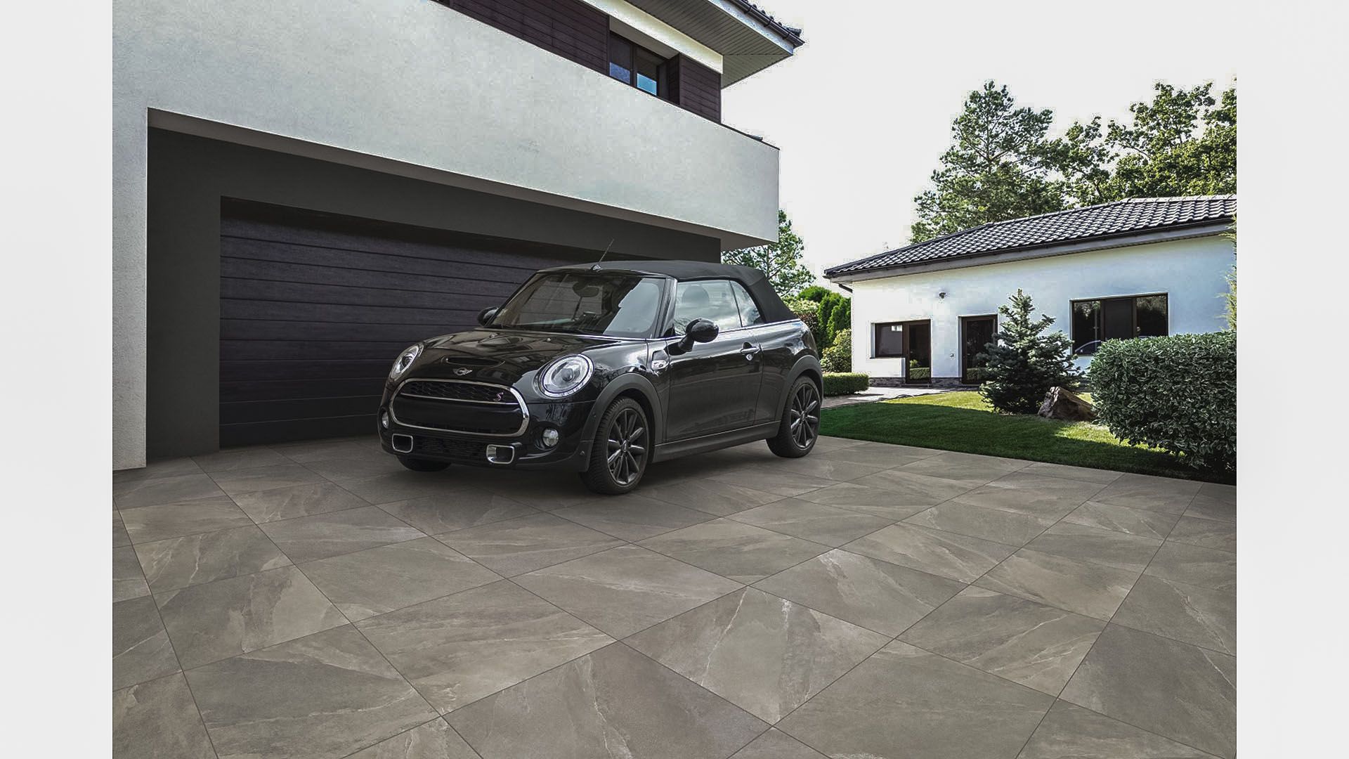 Ein schwarzes Auto parkt in einer gefliesten Einfahrt vor einem Haus.