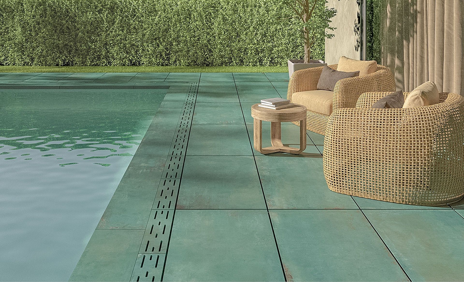 Eine grün geflieste Terrasse mit Korbstühlen und Tisch neben einem Swimmingpool.