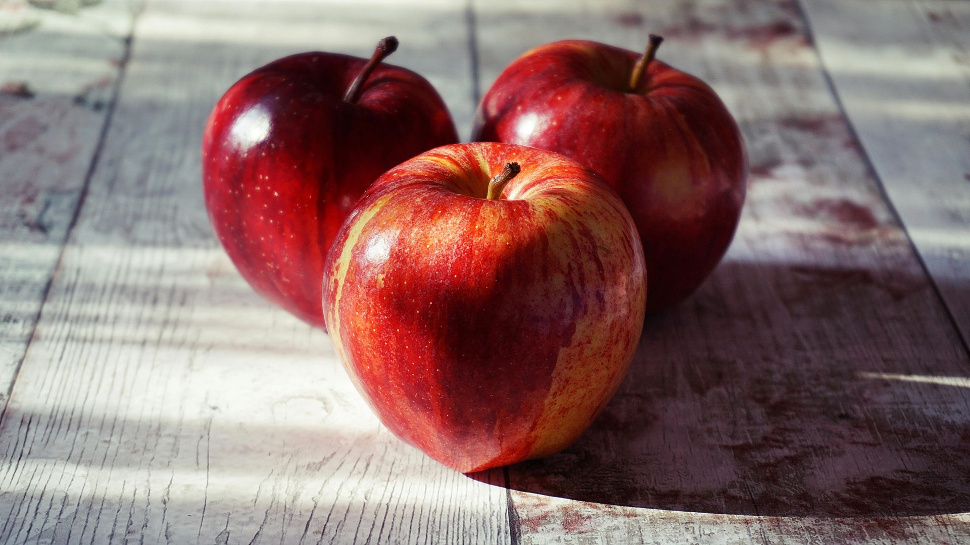 Drei rote Äpfel liegen auf einem Holztisch.