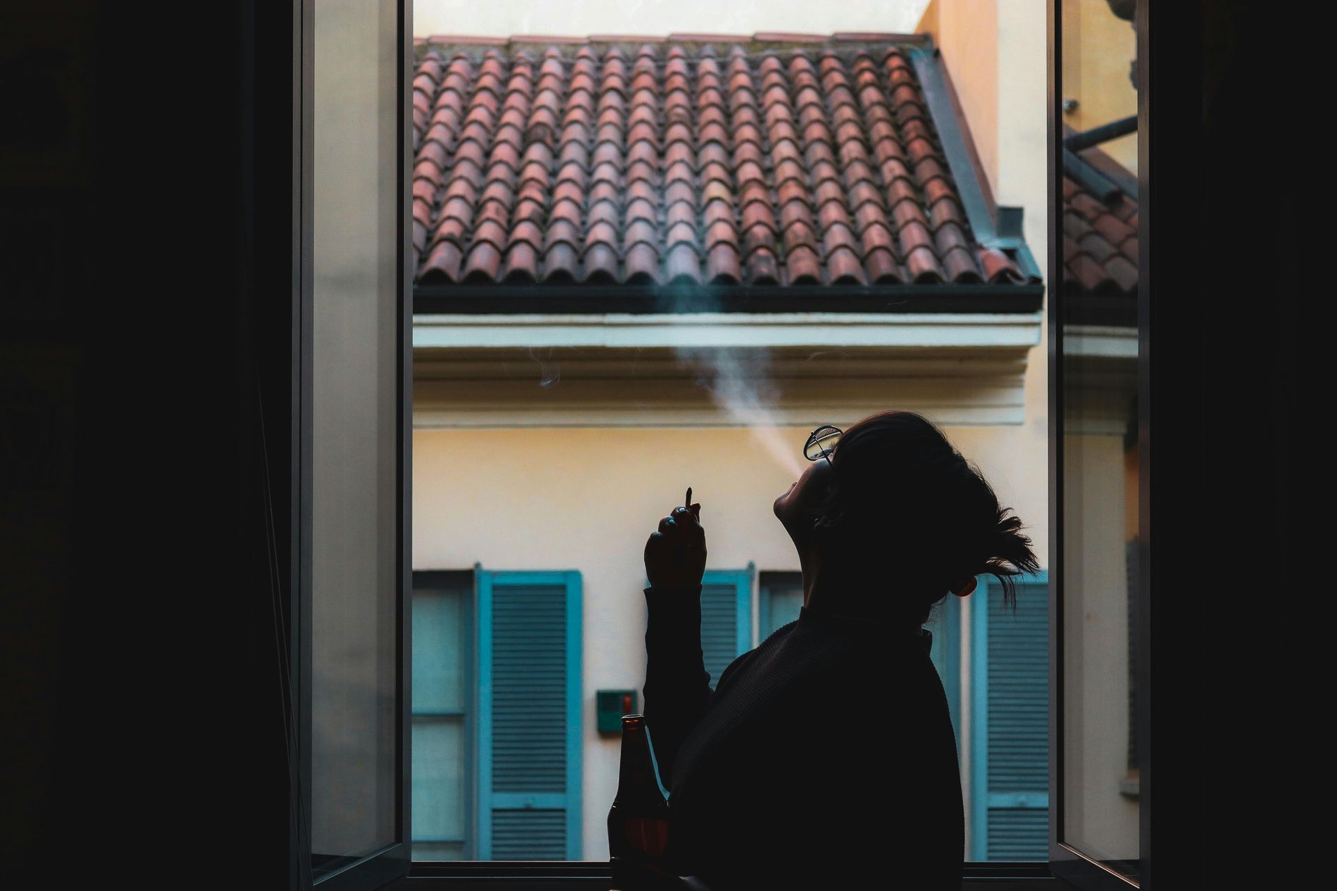 Frau steht am Fenster und raucht