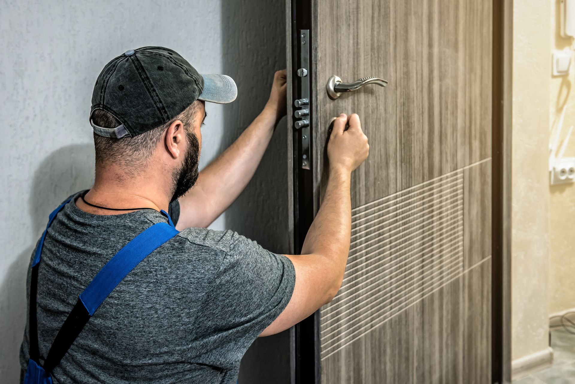 Handyman installing or repairing a door lock, wearing a cap and blue straps.