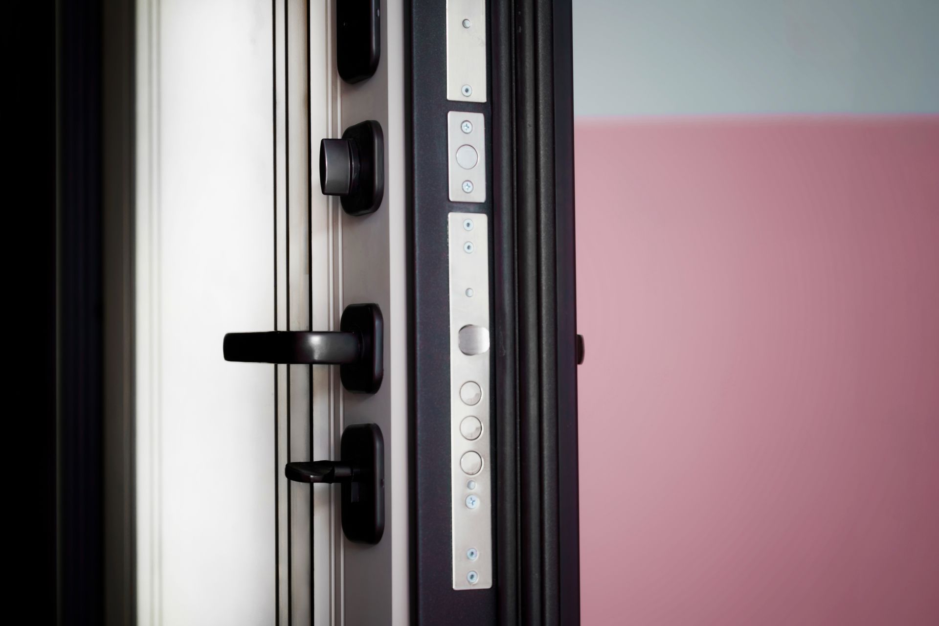 Close-up of a secure, black door with multiple locks and a handle, indoors against pink and white walls.