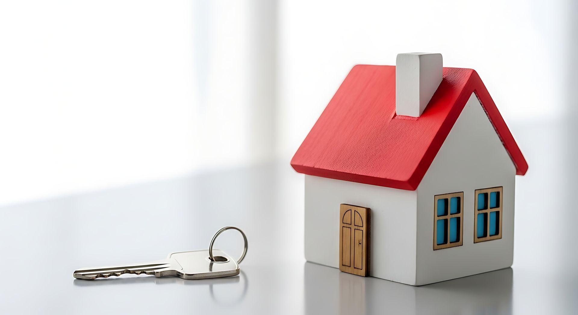 Small house model with a red roof next to a single key on a table.
