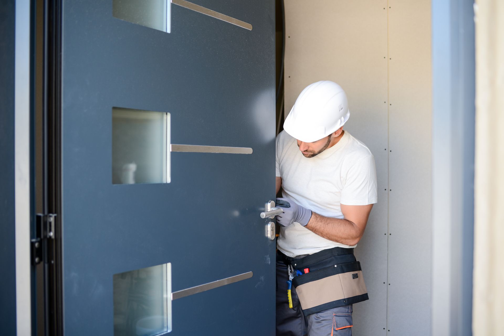 Man in hard hat installing a door handle on a gray door.