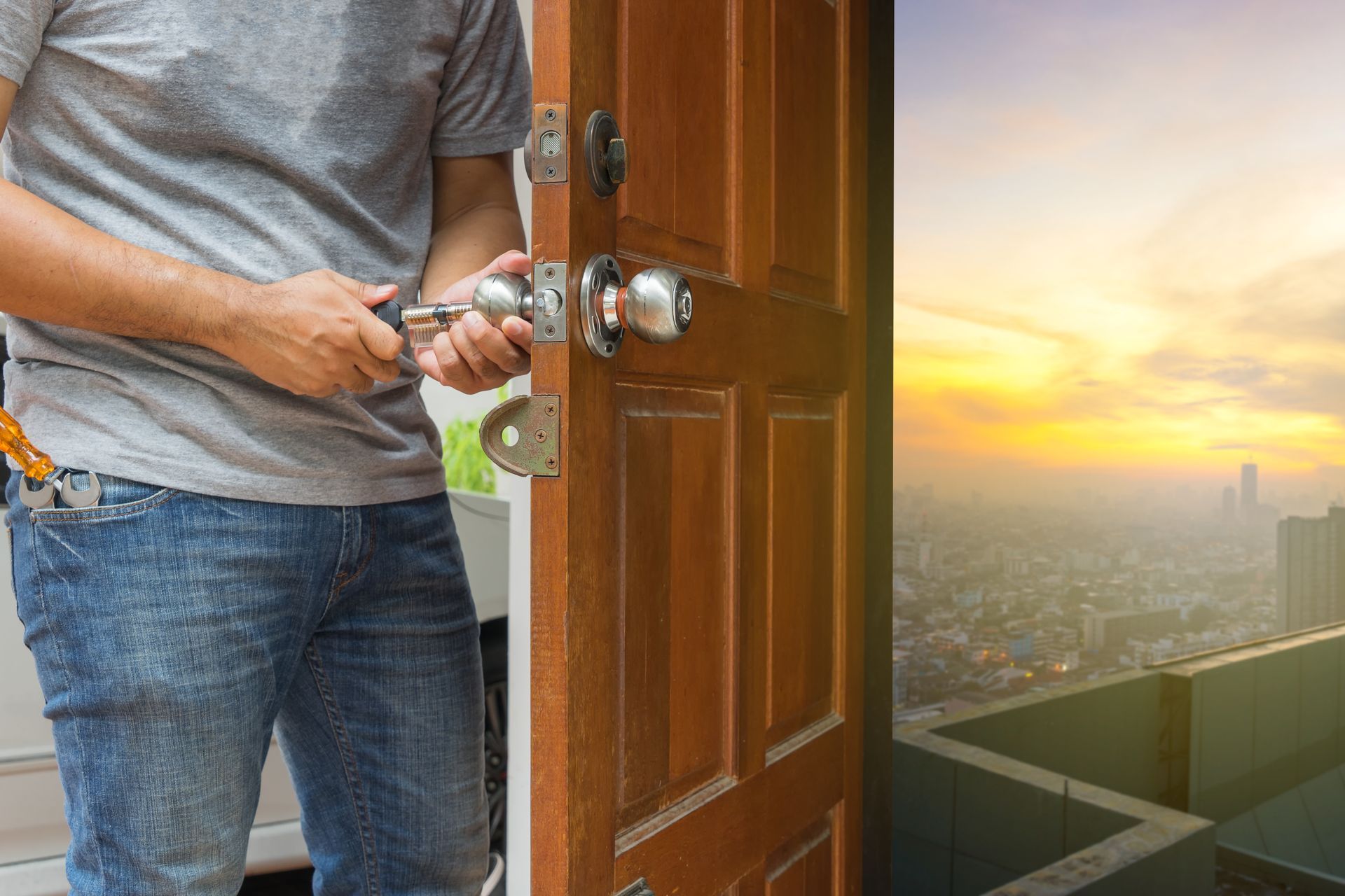 Person fixing a door lock with a screwdriver, open door revealing a cityscape at sunset.