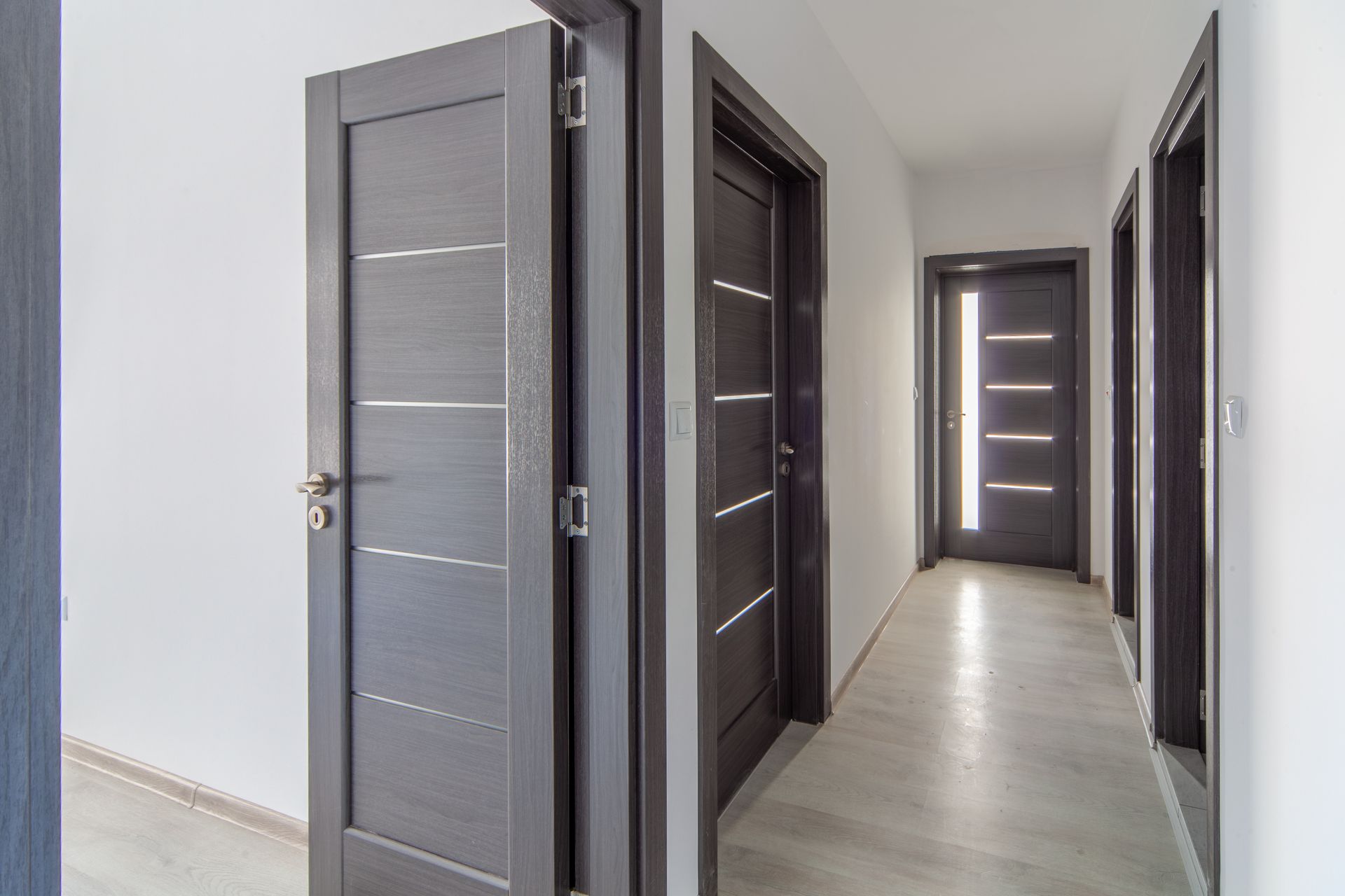 Hallway with grey doors and white walls; one door is open, revealing the interior.