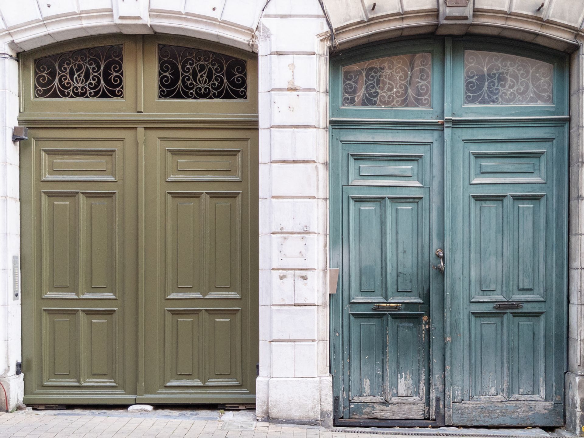Two weathered wooden doors, one olive green, the other teal, set in a stone facade.