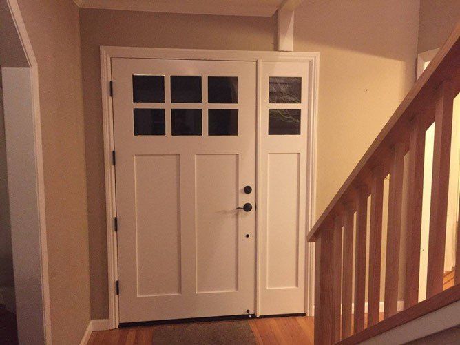 White front door with sidelight and multiple glass panes, beige walls, wooden staircase to the right.