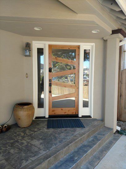 Exterior view of a home's entryway featuring a wooden door with glass panels, flanked by sidelights and steps.