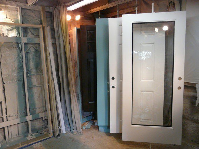 Several painted doors in a workshop, various colors hanging from overhead supports.
