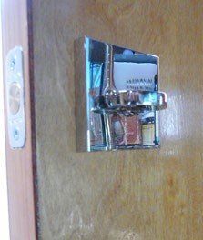 Chrome door lock with a white light switch on a wooden door.