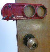 Red lock device attached to a closed wooden door above a doorknob.
