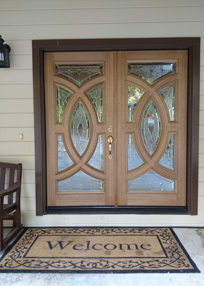 Double wooden front doors with decorative glass panels; a welcome mat.