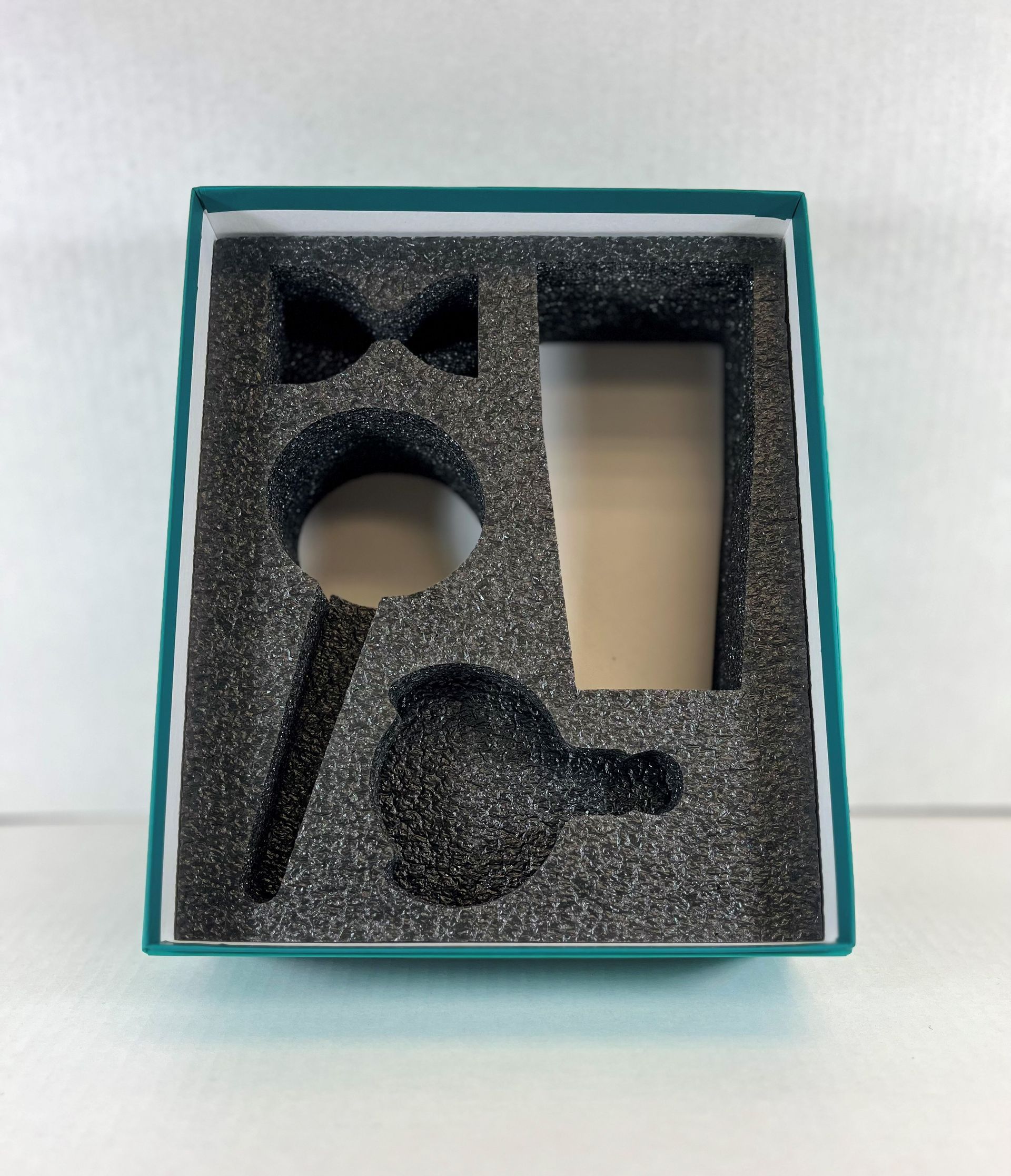 A teal box with black foam insert holds cutouts for small objects.