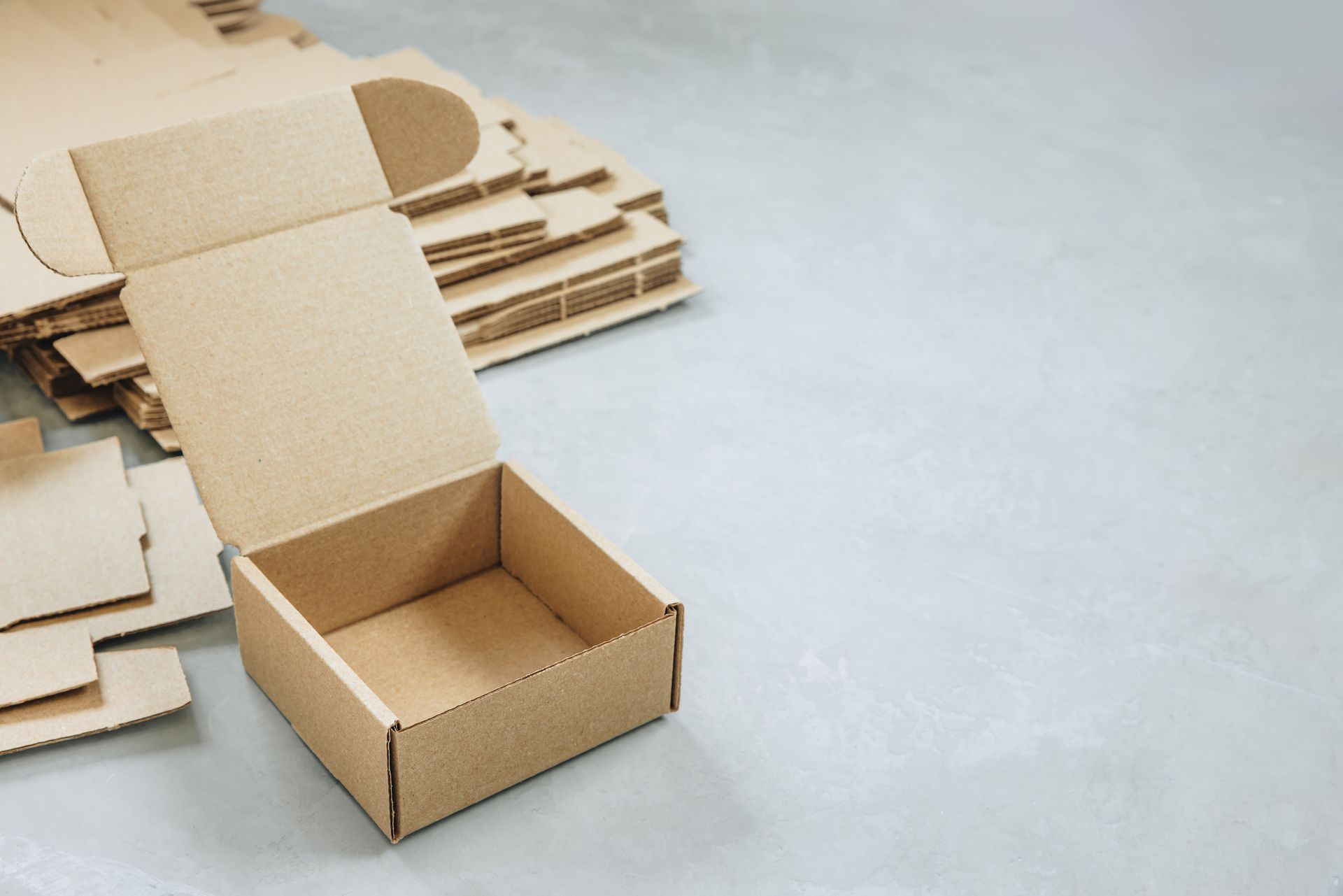 Open cardboard box with flat-packed boxes on gray surface. Open cardboard box with flat-packed boxes on gray surface.