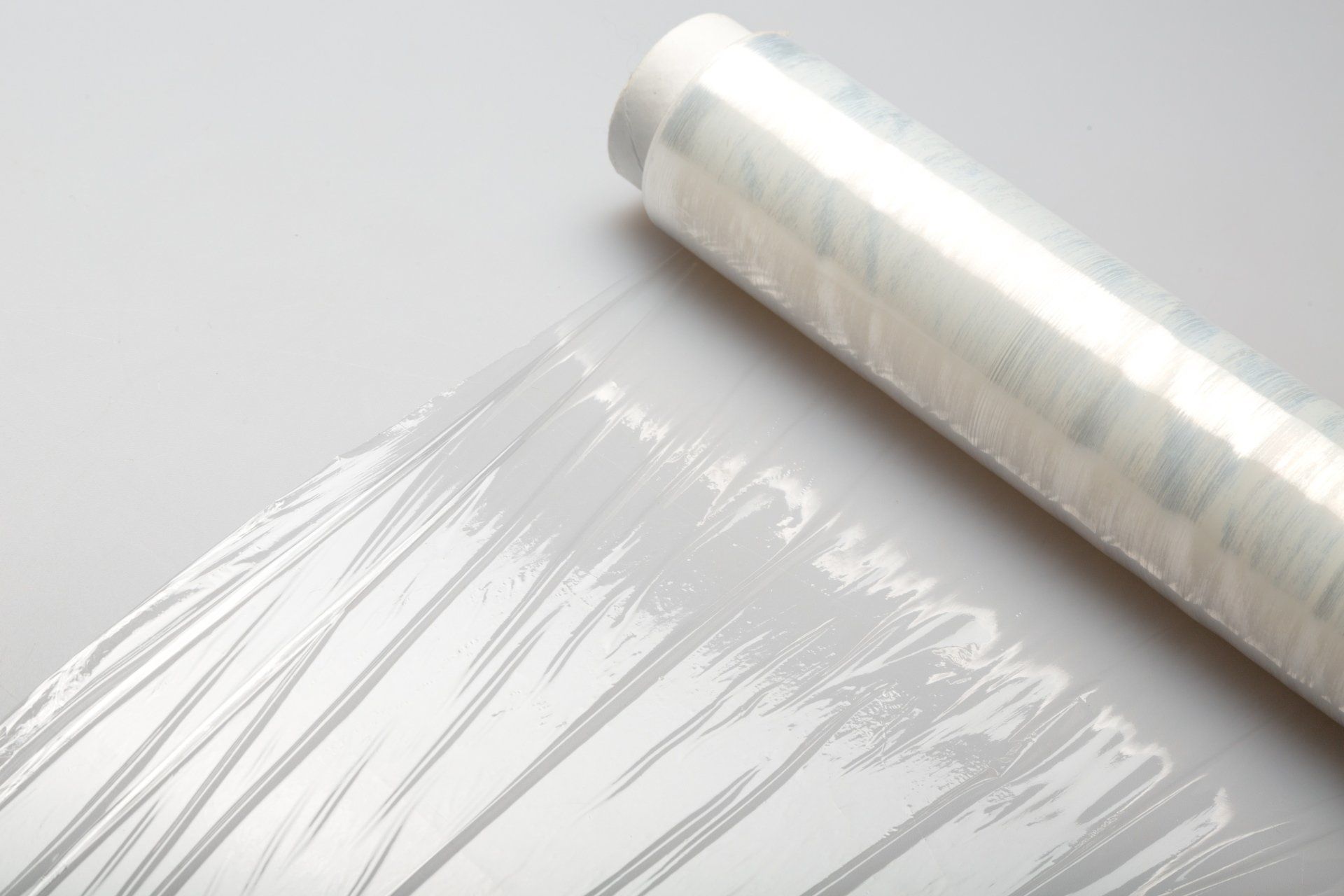 Roll of clear plastic wrap on a white surface with a sheet pulled out.