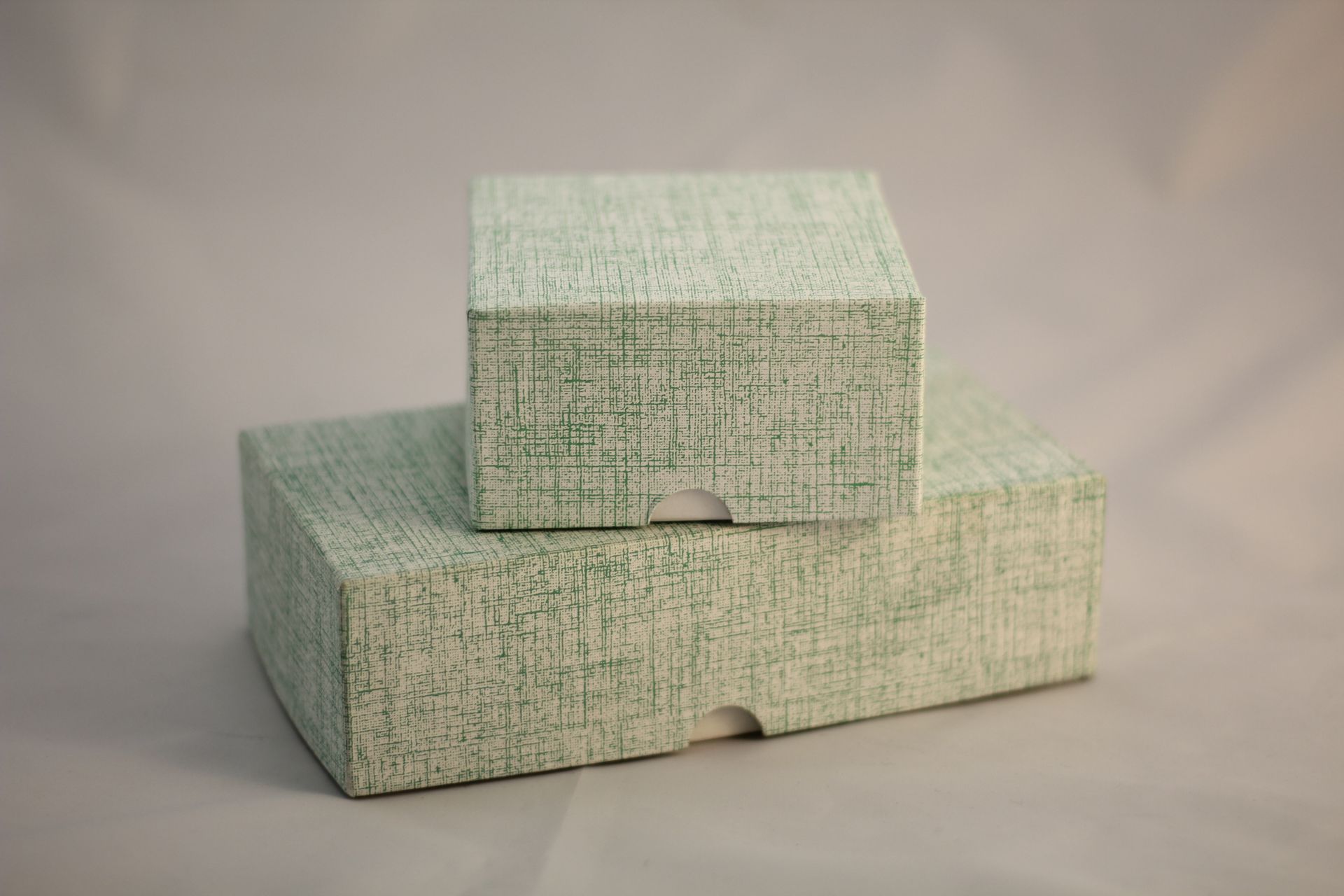 Two textured light green boxes, one stacked atop the other, on a neutral background.