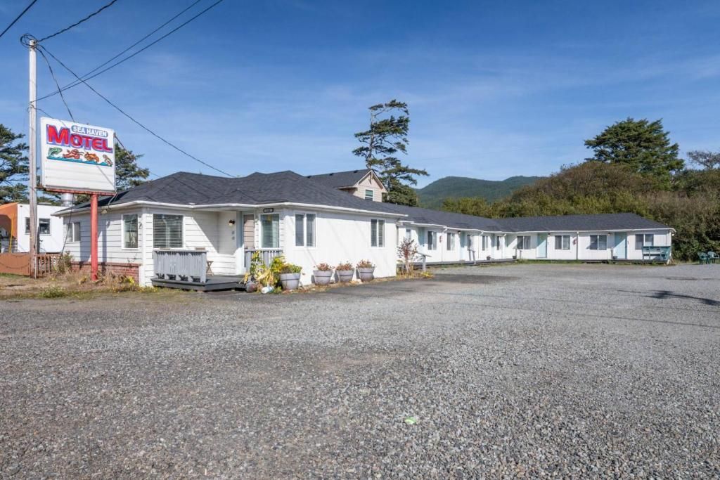 White motel with a red sign, surrounded by a gravel parking lot under a clear blue sky.