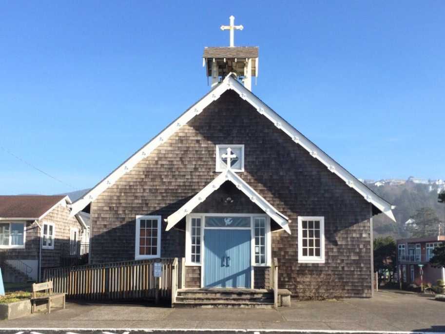 Weathered wooden church with blue doors and a white cross on top.
