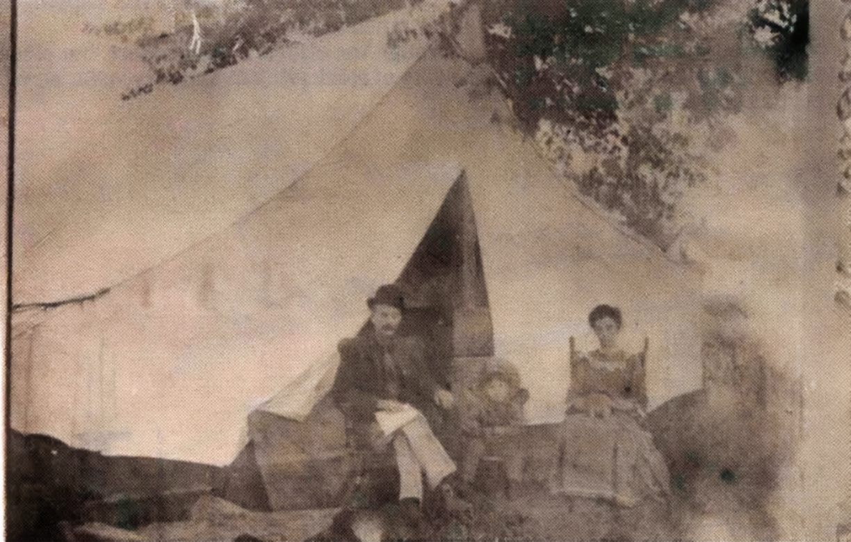 A sepia-toned vintage photo of a steamship passing between two rocky coastal cliffs at the edge of a sandy beach.
