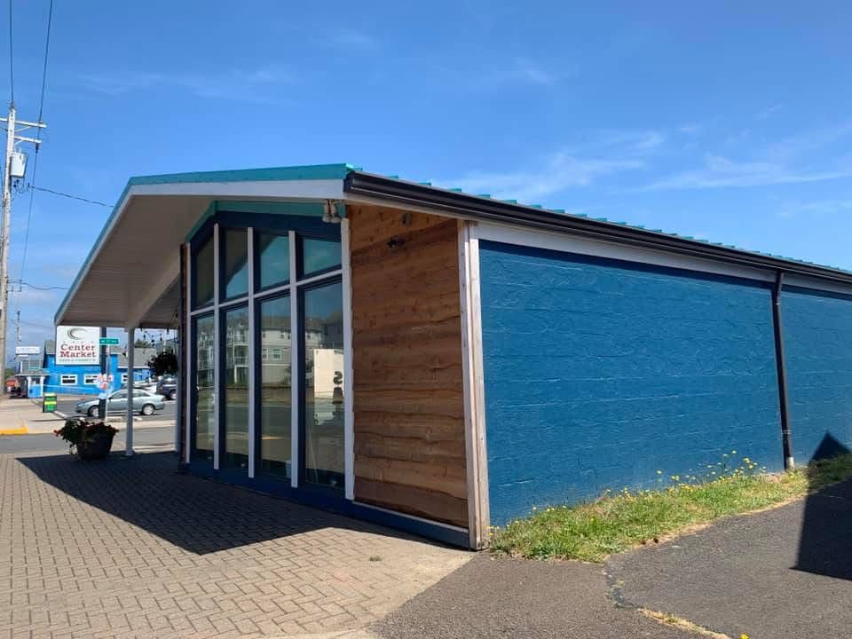 A blue building with large windows and wooden panels on a sunny day.