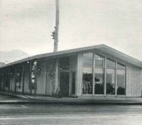 Mid-century modern building with large windows, wood siding, and a sloped roof.
