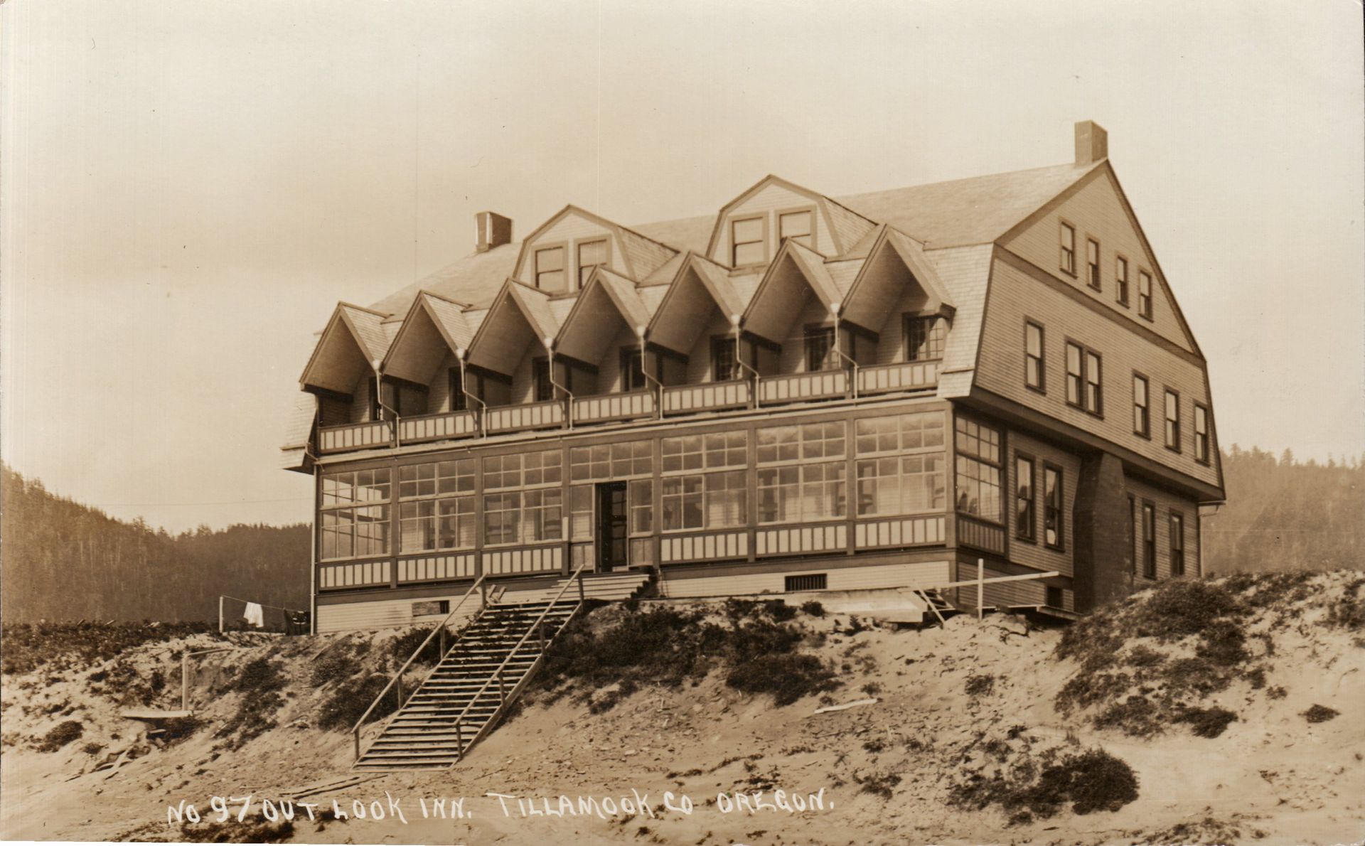 Vintage photo of the Hotel, a large building with a covered porch and unique angled windows on a sandy hillside.