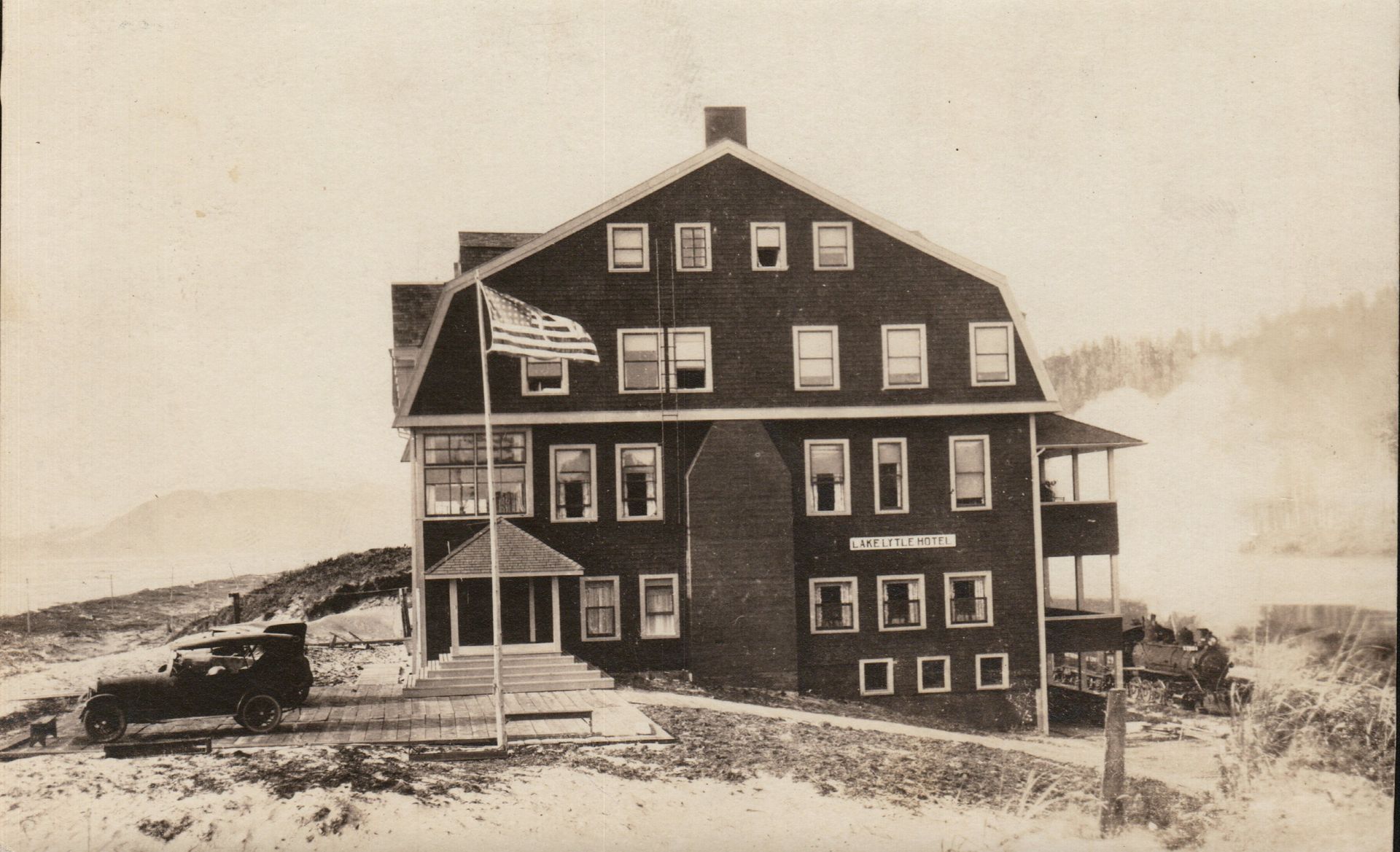 A three-story, dark-colored building with an American flag; a car parked out front.