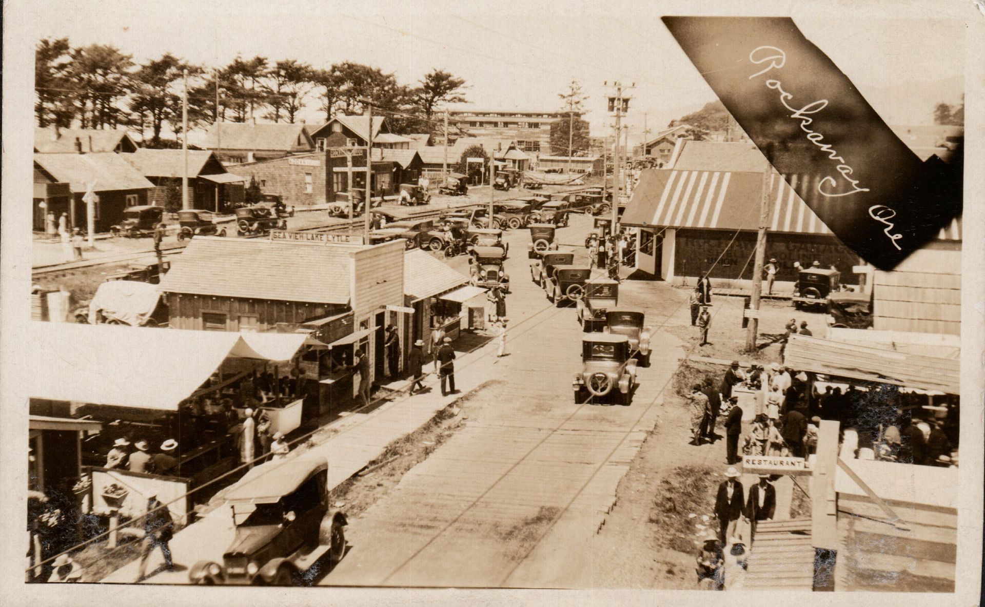 Street view of a town with cars, people, and buildings.