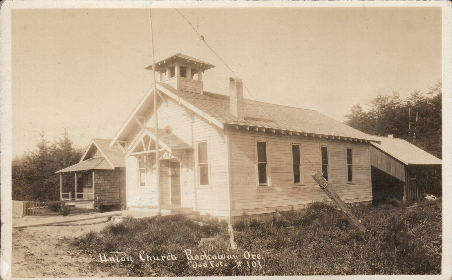Old sepia-toned church with steeple, small porch, and shed. Text on image: 