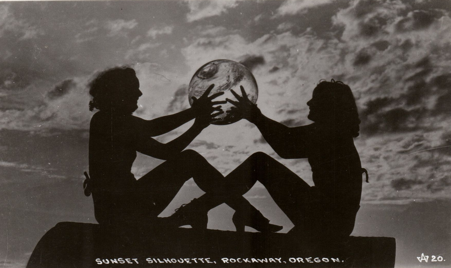 Two people holding a sphere with clouds backdrop, Oregon. Silhouetted figures, black and white photo.