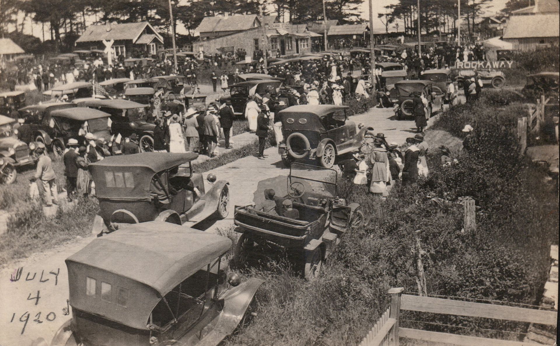 Crowded vintage car gathering in an outdoor park, with many early automobiles parked among people and trees.
