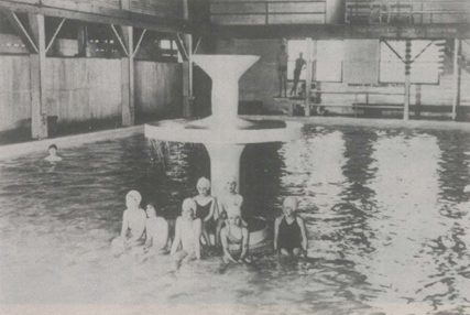 Indoor swimming pool, people in swimsuits grouped near a fountain.