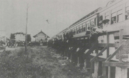 People on train platform next to passenger train.  Old photograph, early 20th century.
