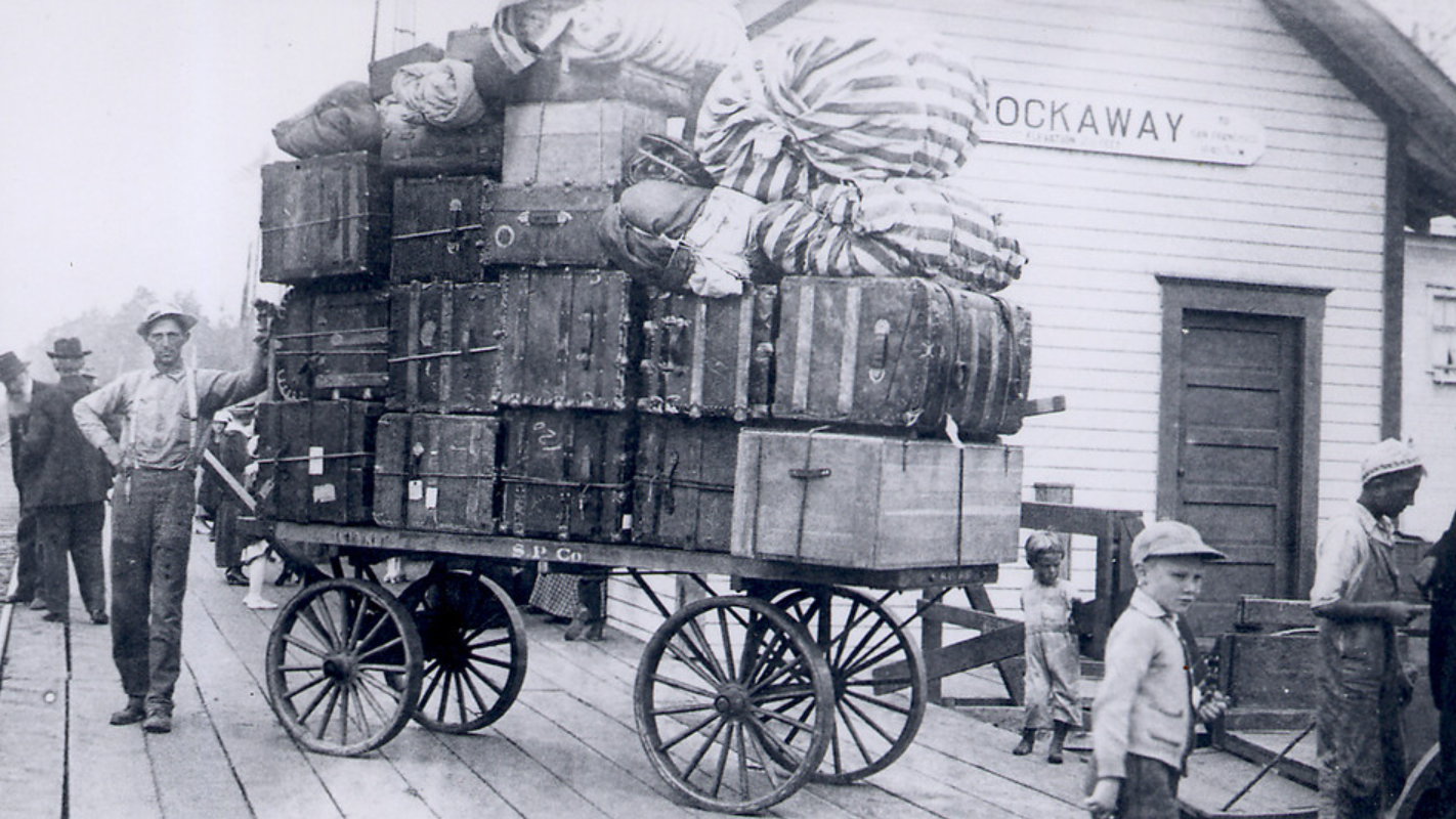 Wagon piled high with luggage at Rockaway station. People nearby.
