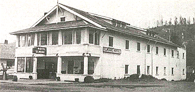 Black and white photo of the Hotel, a large two-story building with a porch and signage, in a rural setting.
