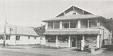 Two-story building with covered porch, storefront on the first floor, and a smaller building to the left.