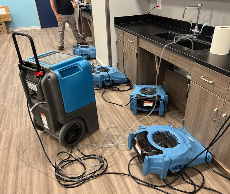 Dehumidifiers drying a wet room near a sink and cabinets. A person stands nearby.