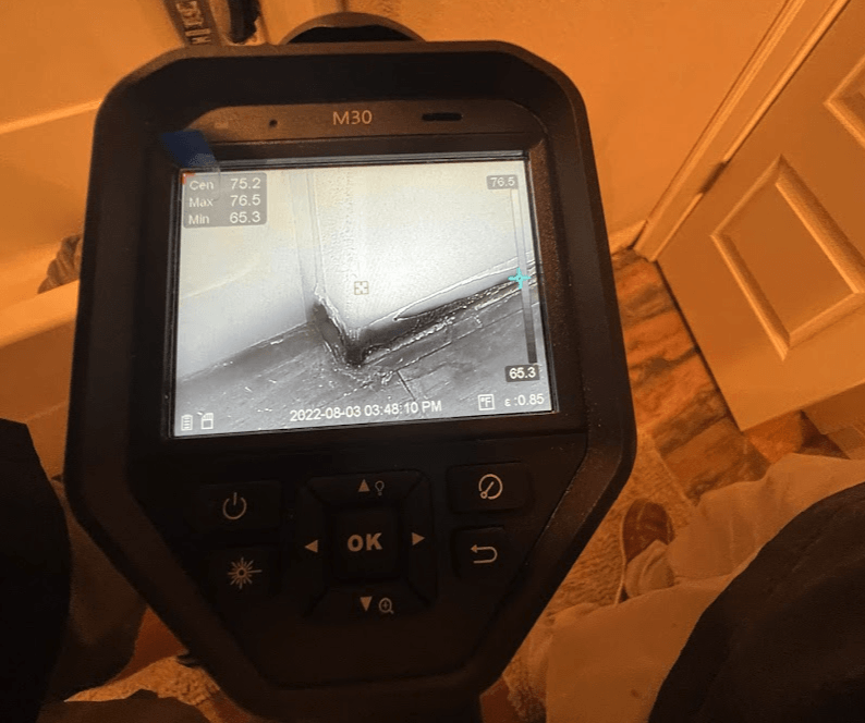 A thermal imaging camera displays a view of a wall's corner; the user is holding the device.