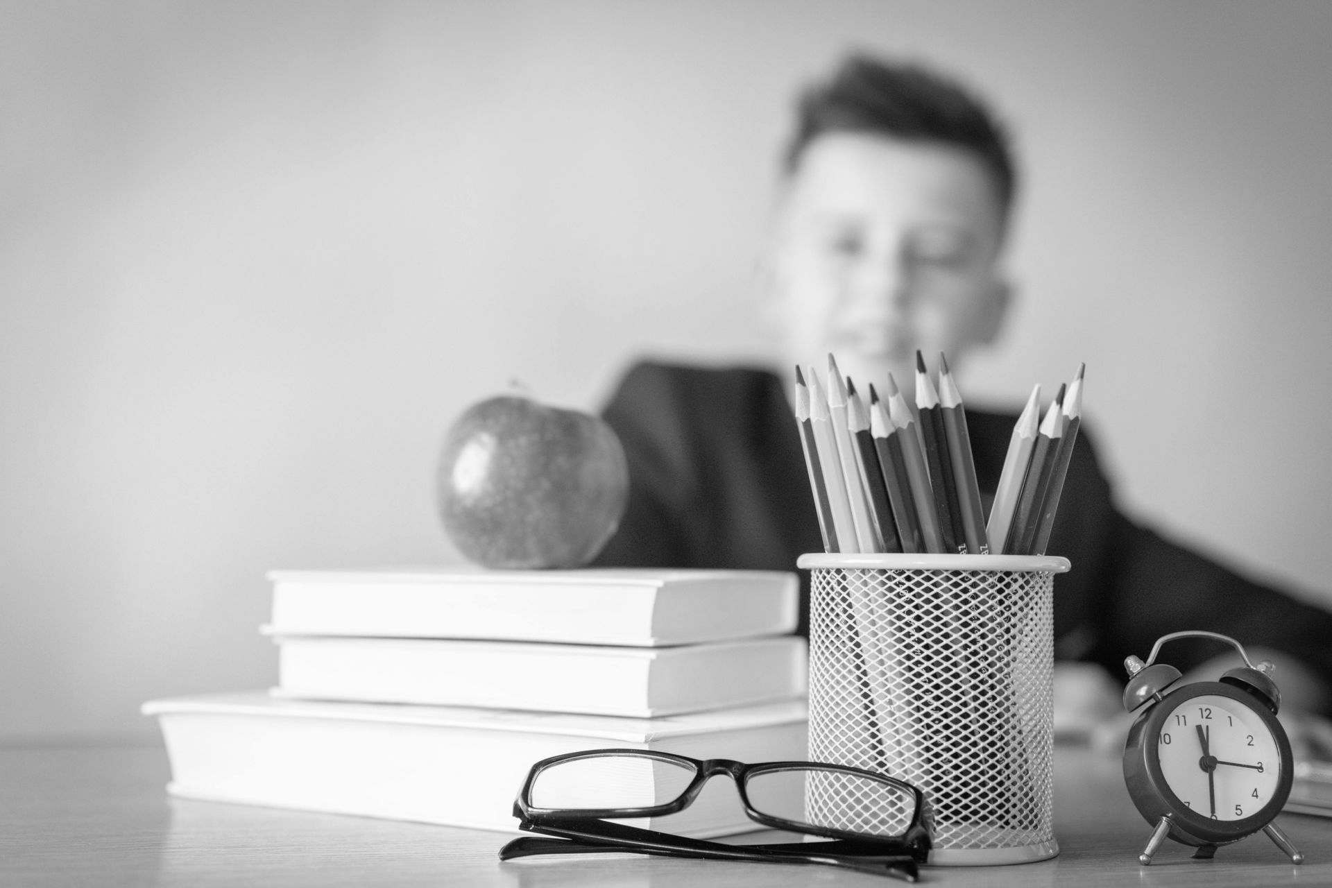 Boy writing in a notebook at a table, pencil in hand. Black and white photo.