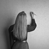 Woman writing on a wall with a pencil; long hair, back view.