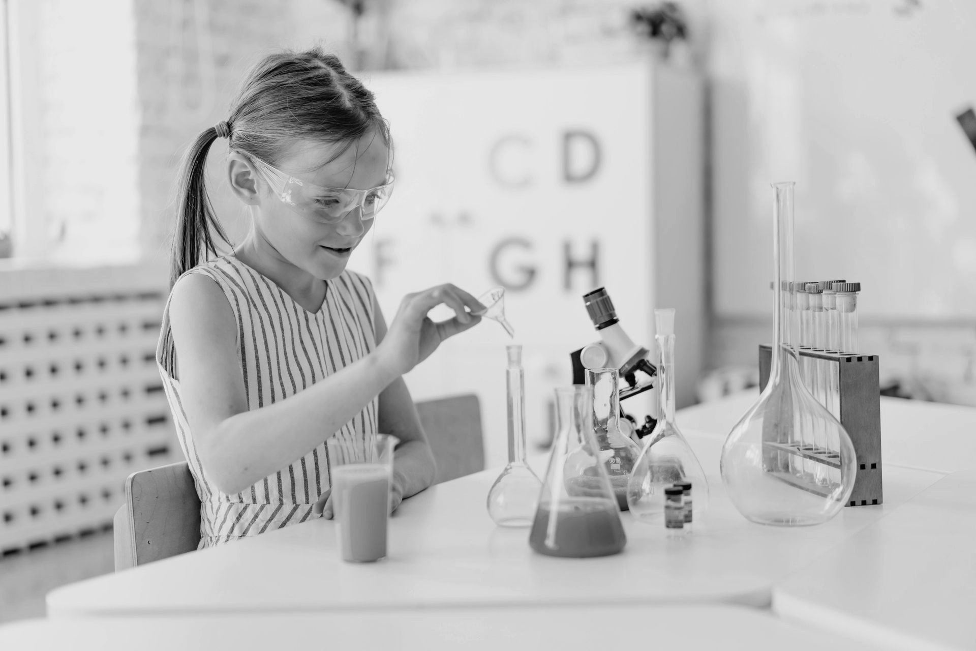 Young girl in goggles, experimenting with liquids in a science lab, using a dropper and beakers.
