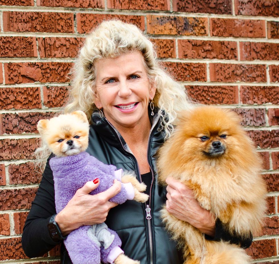 Woman holding two fluffy Pomeranians in front of a brick wall