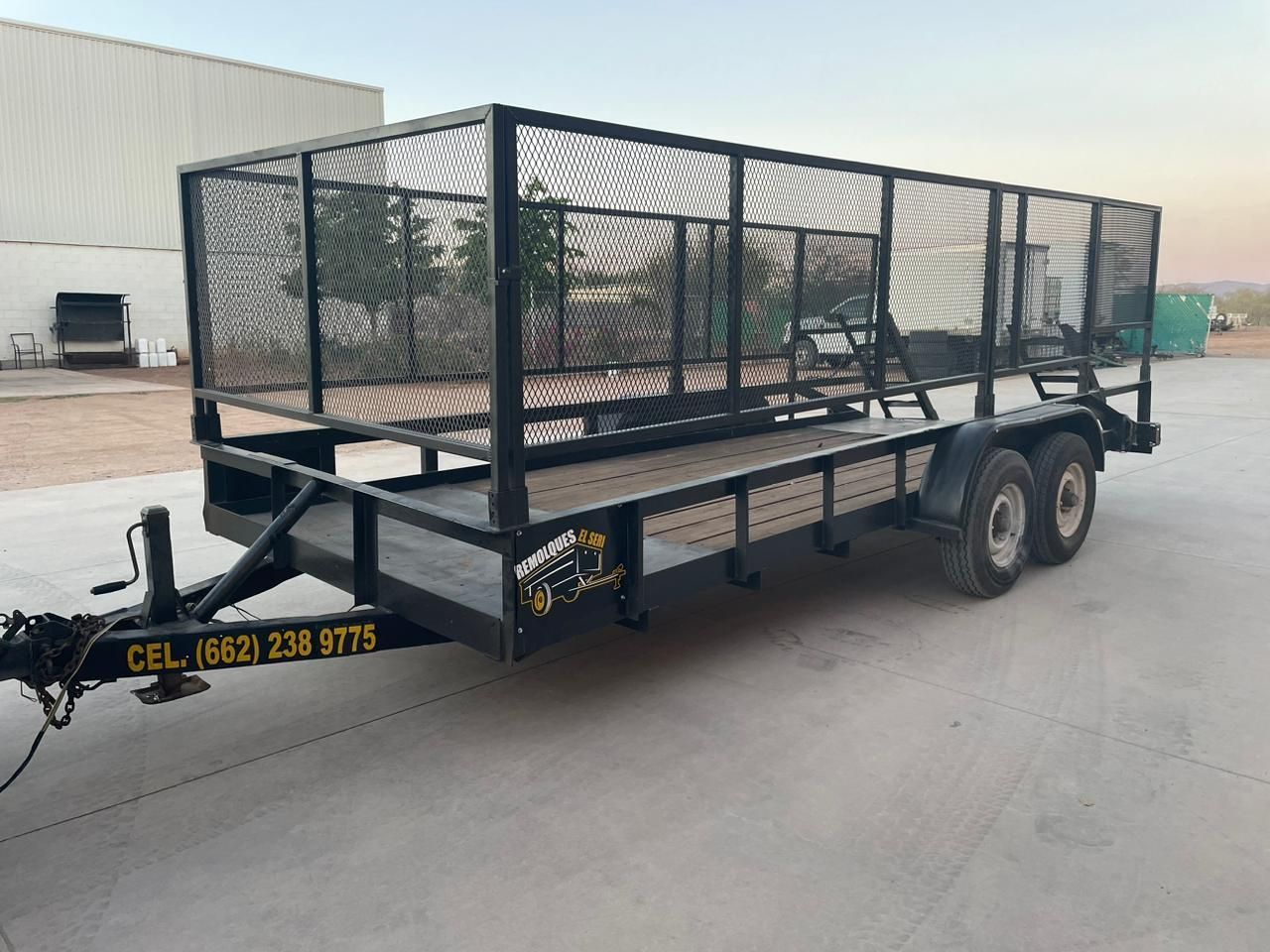 Un remolque con una jaula encima está estacionado en un estacionamiento.