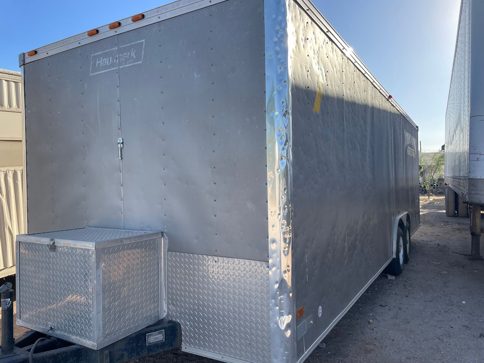 Un remolque gris está estacionado al lado de un remolque blanco.