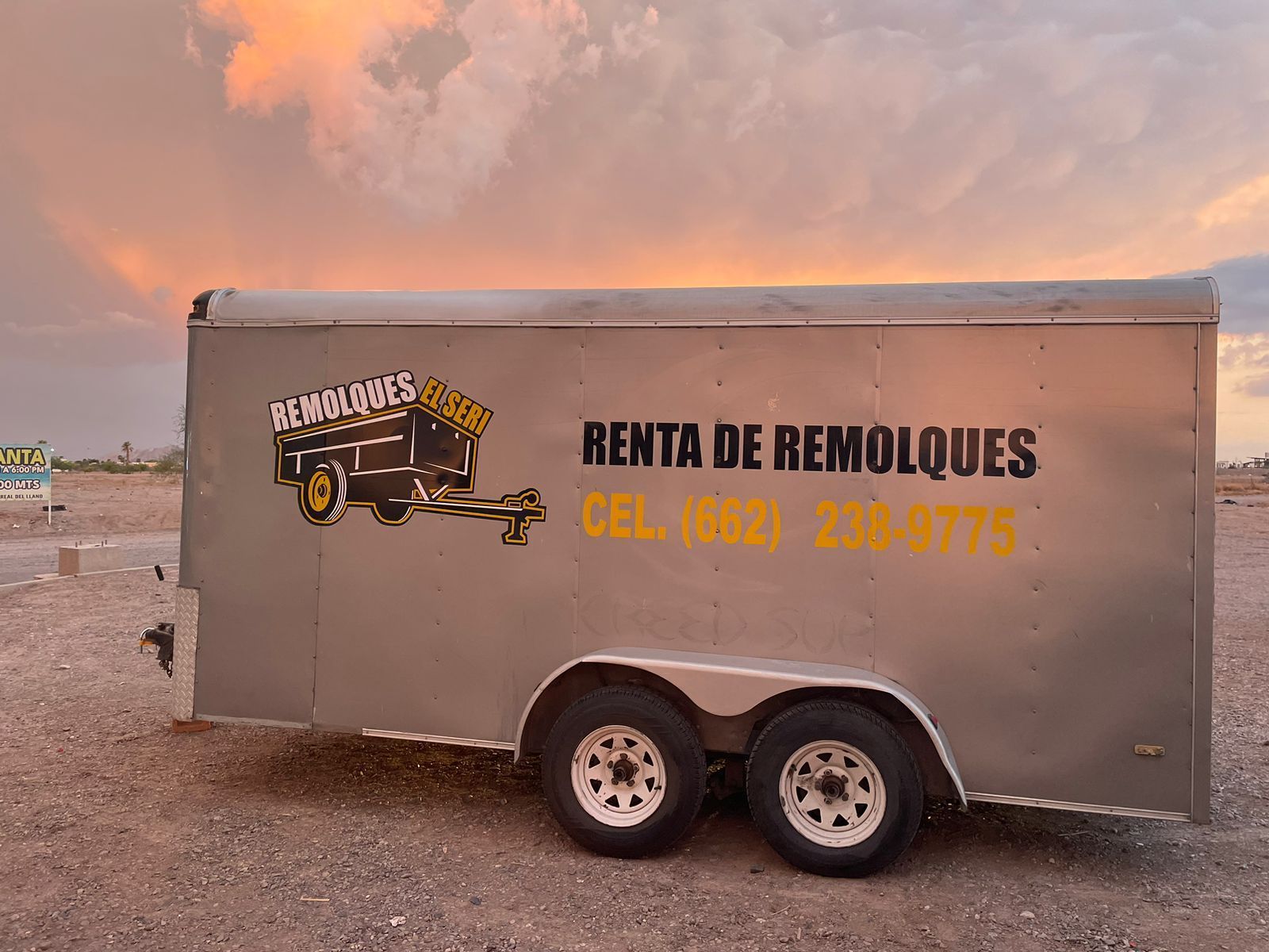 Un remolque está estacionado en un campo de tierra con una puesta de sol de fondo.